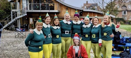 Racks Out women's eight posing in font of the boat house dressed as elves, with the cox as Santa