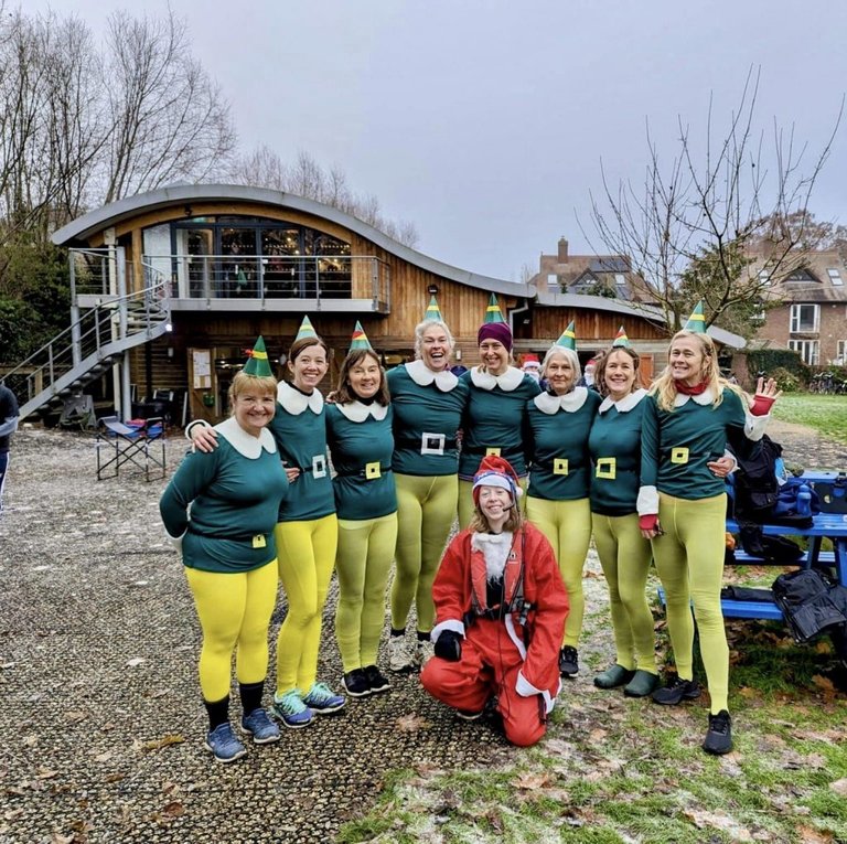 Racks Out women's eight posing in font of the boat house dressed as elves, with the cox as Santa